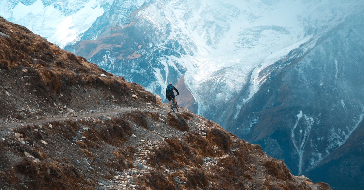 Cyclist on rugged mountain trail in Khangsar, Nepal with snow-capped peaks.